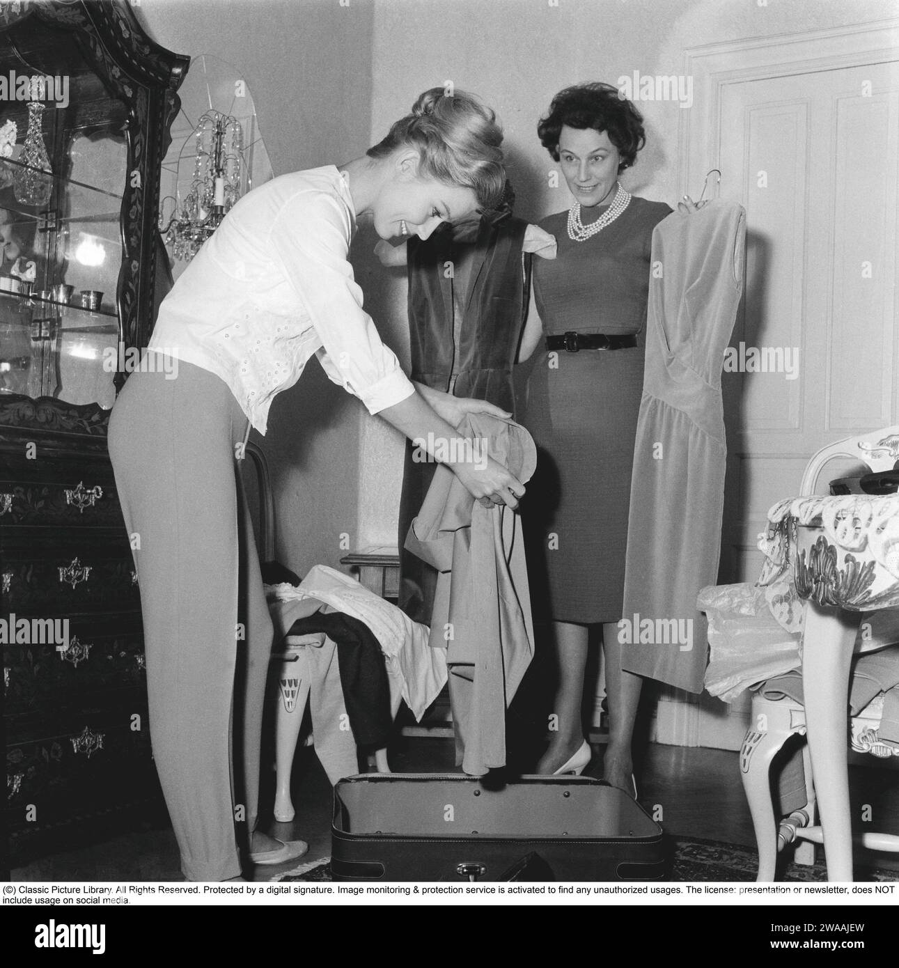 In the 1960s. Two women are packing a suitcase with clothes. 1960 Stock Photo