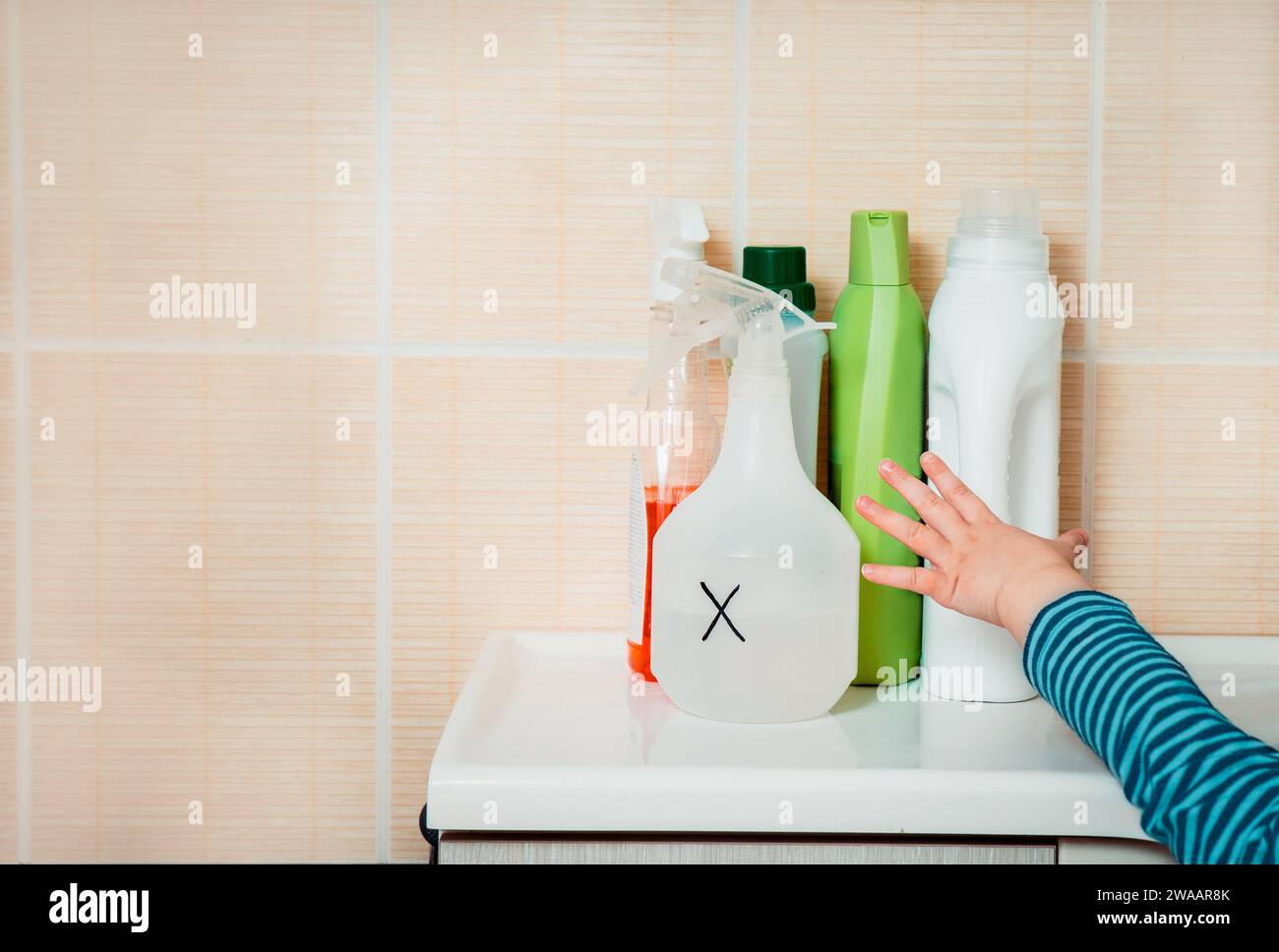 Little child reaches out to household chemicals. Keep away from children. Dangers at home for kids. Stock Photo