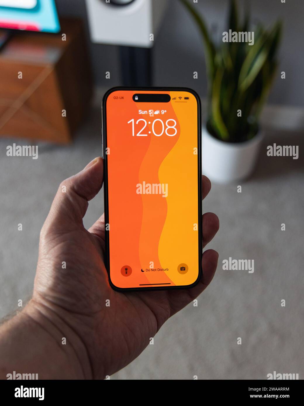 LONDON - NOVEMBER 05, 2023: Apple iPhone 14 Pro held in hand with bright orange color wallpaper on screen Stock Photo