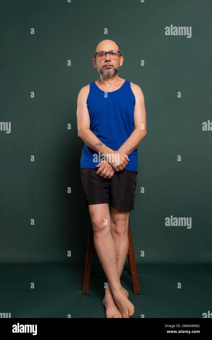 White man in a blue shirt and black shorts, standing, posing for a photo against a dark green background. Stock Photo