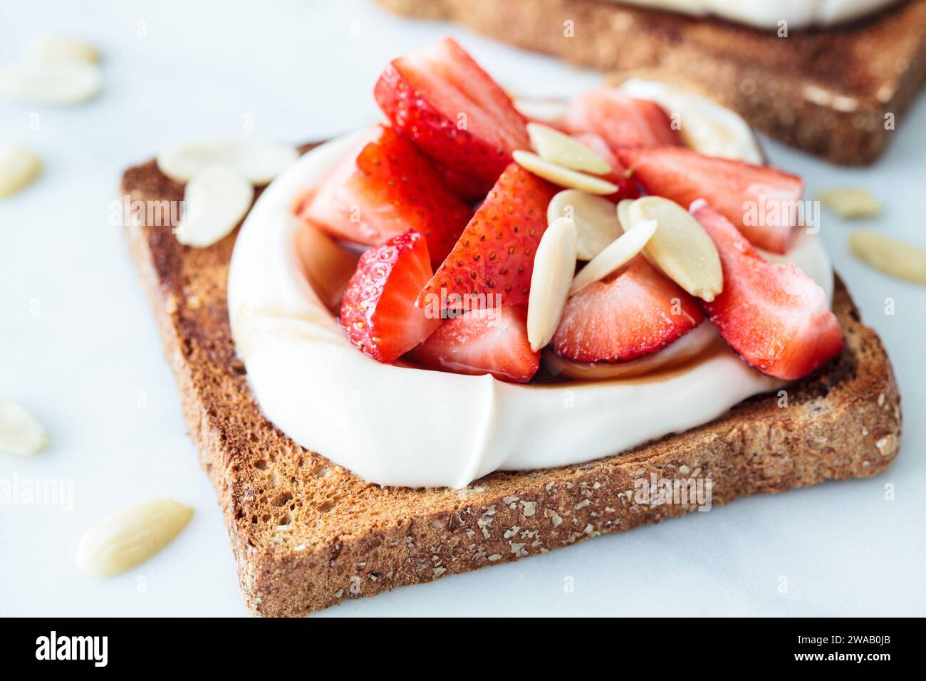 Crispy breakfast toast with ricotta, strawberries and almonds on a white marble background. Stock Photo