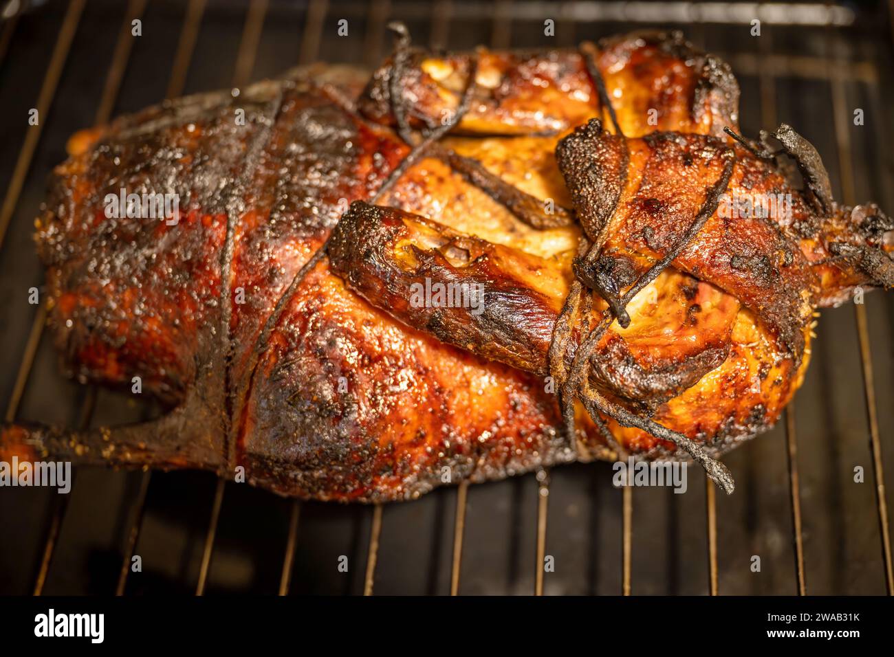 Whole roasted peking duck on baking grid, body tied up, chinese cuisine, closeup. Stock Photo