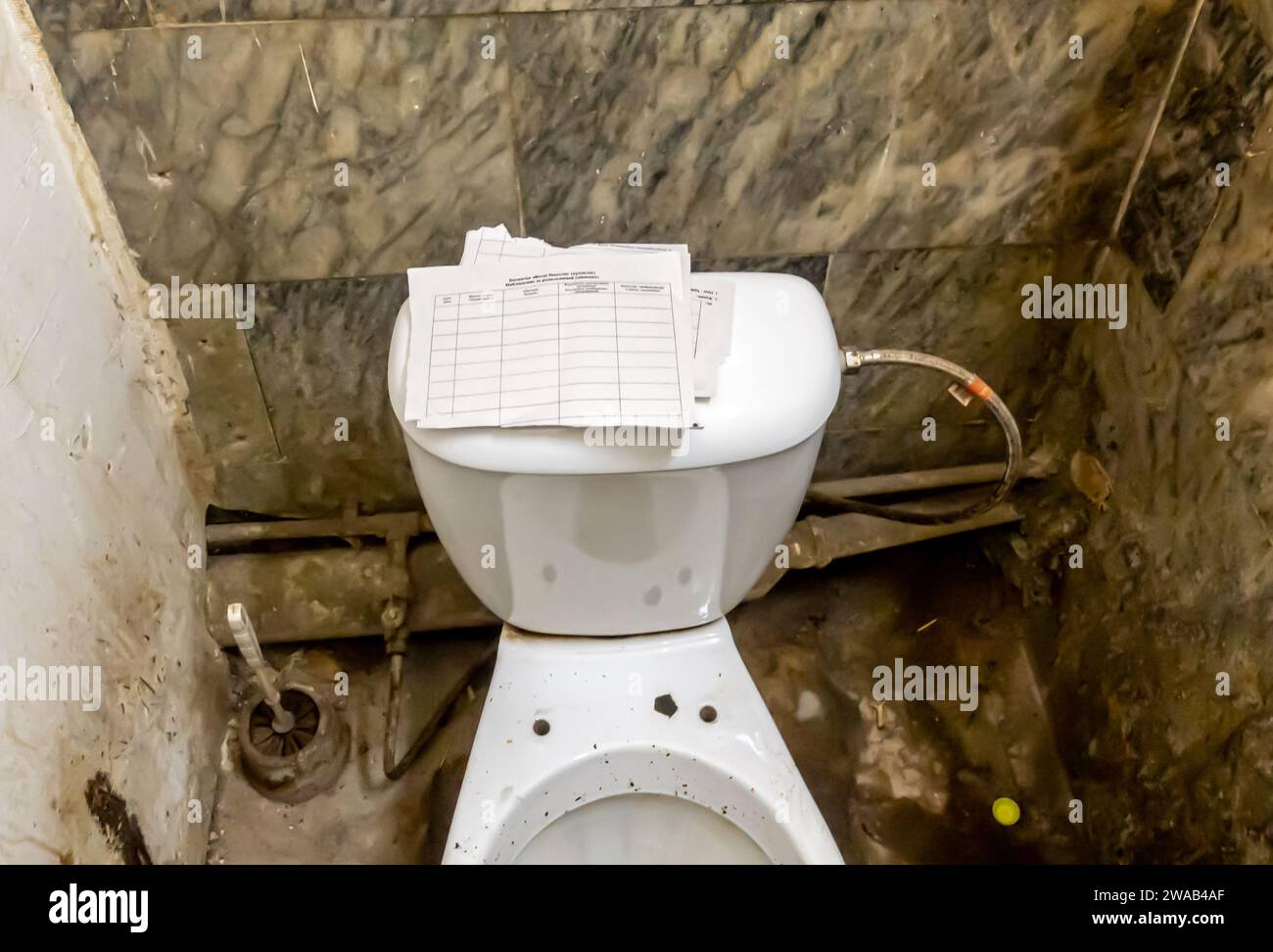 Bathroom toilet arrangement typical for public restrooms in the Soviet time, with a torn paper as toilet paper Stock Photo