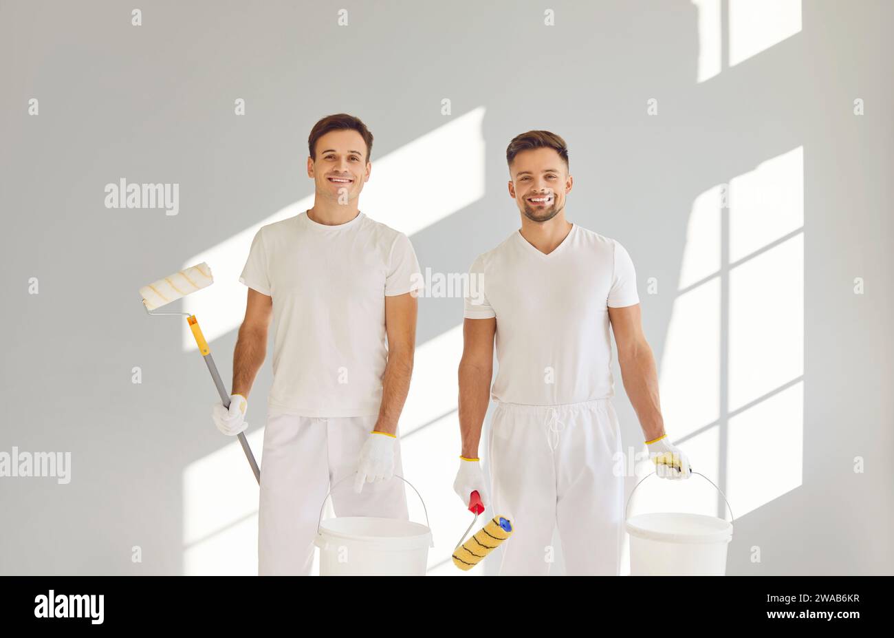 Paint Roster Team of house painters looking at camera holding paint rollers and ...