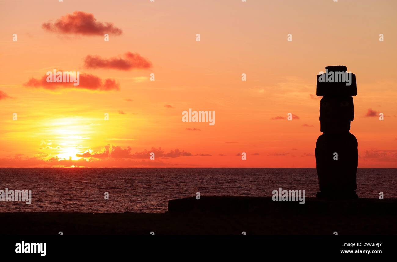 Silhouette of Moai wearing hat called Pukao at Ahu Ko Te Riku ceremonial platform against stunning sunset sky, Pacific ocean, Easter island, Chile Stock Photo