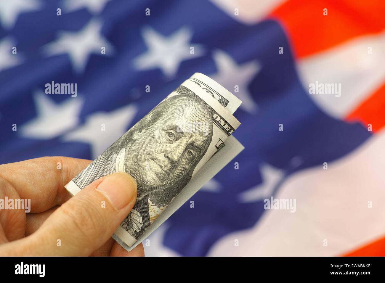 A person holding a one hundred dollar bill above the flag of the USA. Close up. Stock Photo