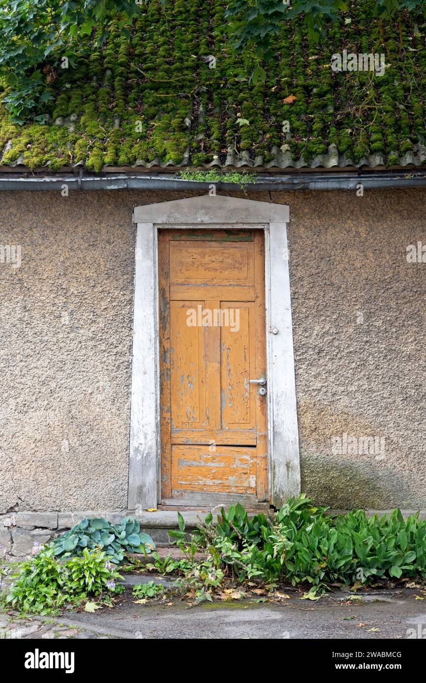 Gray stucco house with moss growing on terracotta roof tiles, yellow-orange wood-panelled doorway with white trim, Viljandi, Estonia. Stock Photo