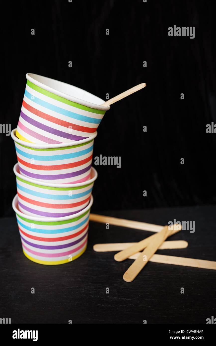 A stack of colorful striped paper cups and wooden stirrers on a black ...