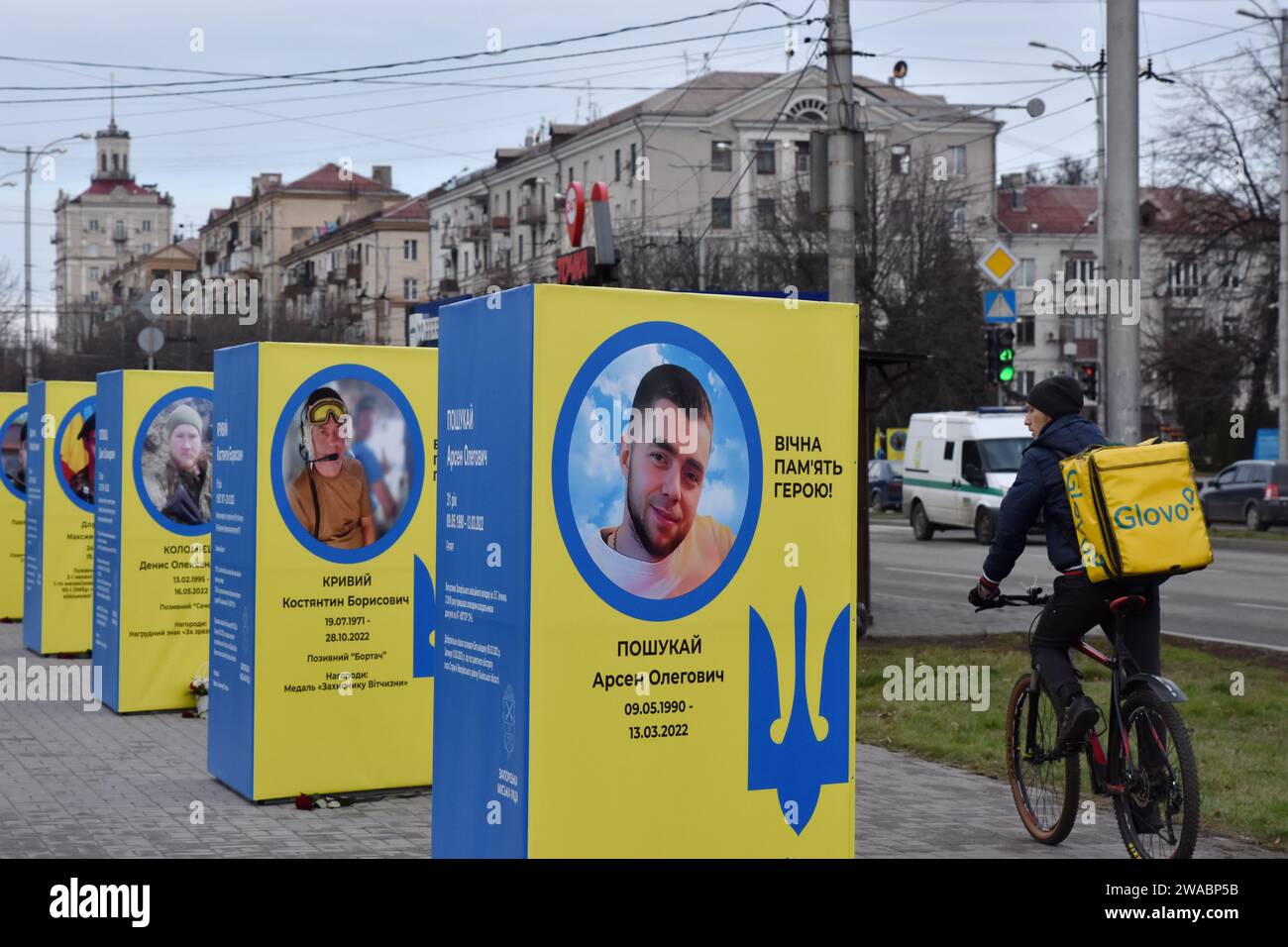 A man from delivery service rides a bicycle past stands of portraits of fallen Ukrainian soldiers in the center of Zaporizhzhia. Ukrainian President Volodymyr Zelenskiy said Russian forces are suffering heavy losses and the notion that Moscow is winning the nearly two-year-old war is only a 'feeling' not based on reality. There was no response to a request for comment from Russian officials on Zelenskiy's remarks. Russian officials have said Western estimates of Russian death tolls are vastly exaggerated and almost always underestimate Ukrainian losses. Stock Photo