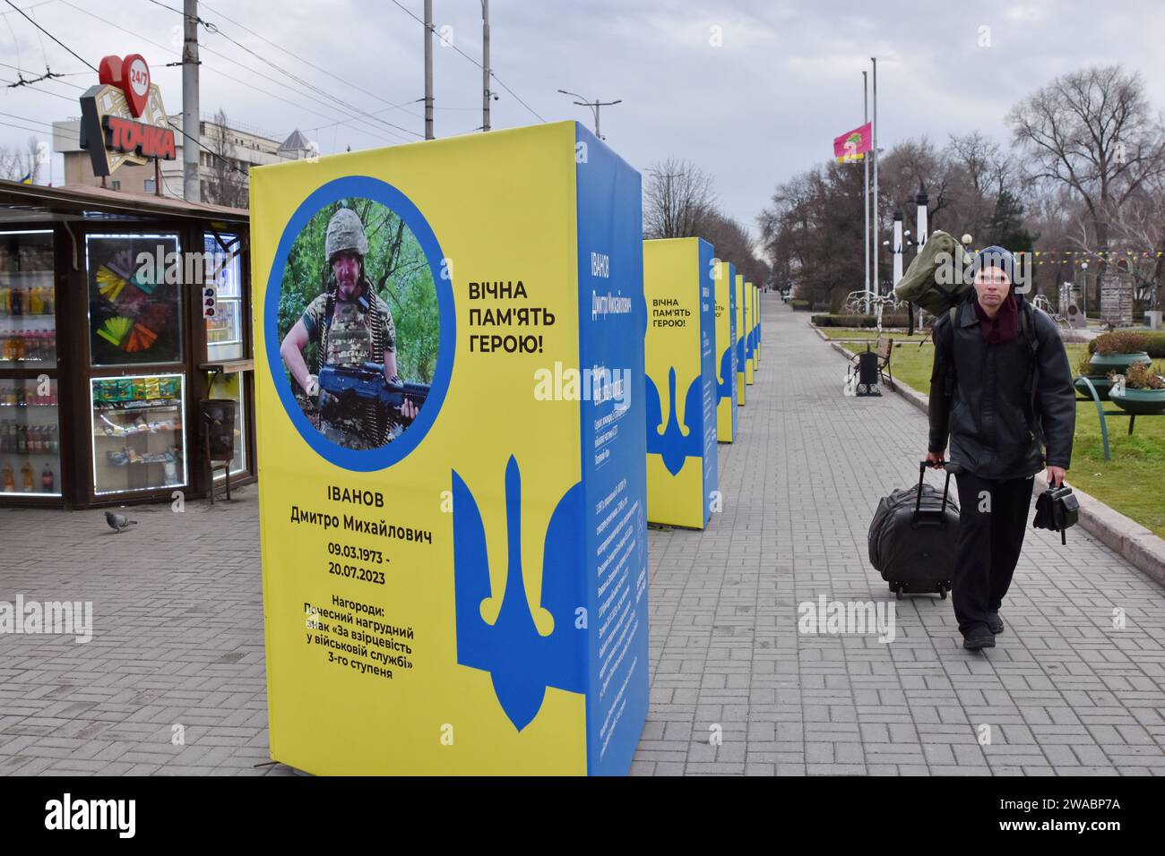 A man walks with his suitcase and backpack past stands of portraits of fallen Ukrainian soldiers in the center of Zaporizhzhia. Ukrainian President Volodymyr Zelenskiy said Russian forces are suffering heavy losses and the notion that Moscow is winning the nearly two-year-old war is only a 'feeling' not based on reality. There was no response to a request for comment from Russian officials on Zelenskiy's remarks. Russian officials have said Western estimates of Russian death tolls are vastly exaggerated and almost always underestimate Ukrainian losses. Stock Photo