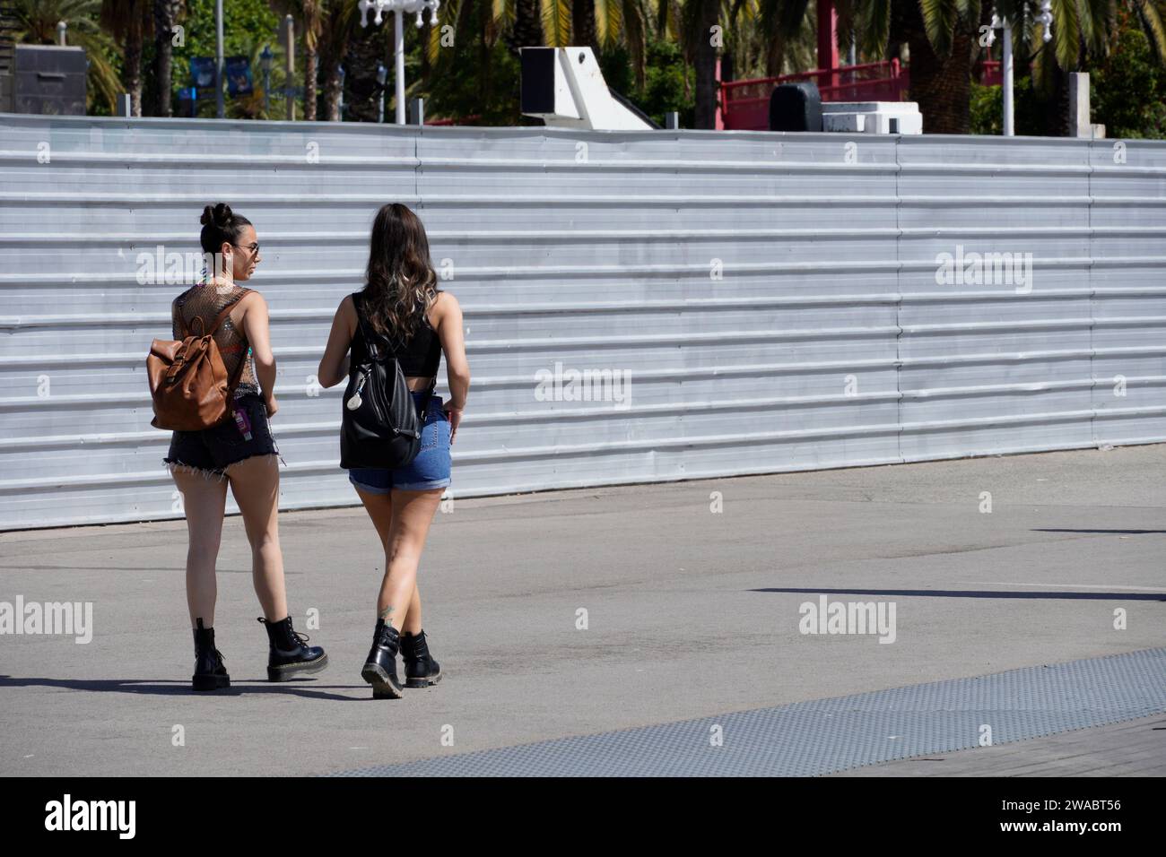 Barcelona, Spain - May 26, 2022: Two stylish young girls walk through the construction zone dressed in jean shorts and military boots, both carrying b Stock Photo
