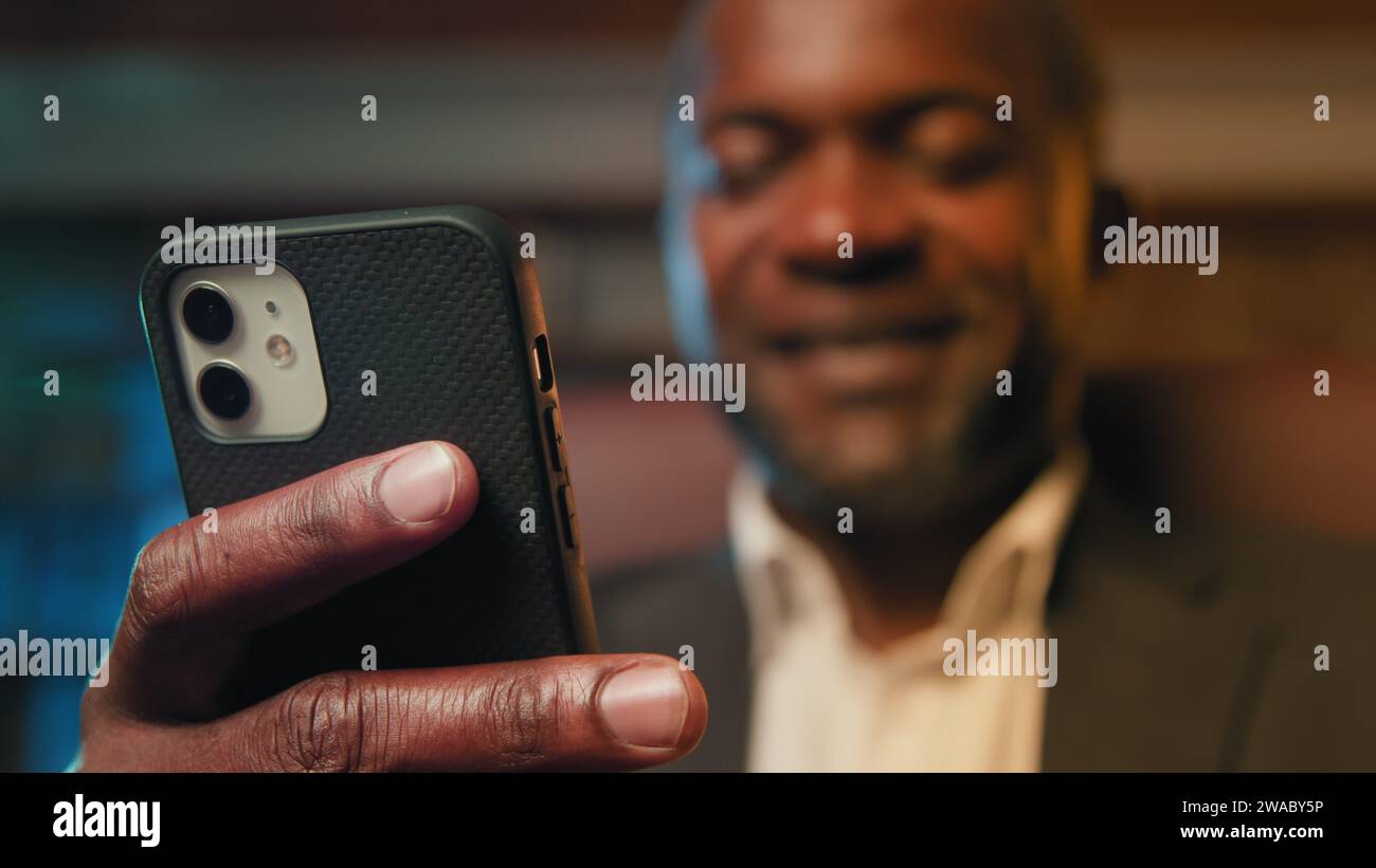 Blurred focus african american businessman holding smartphone browsing social network writing email message happy man chatting remotely communicating Stock Photo