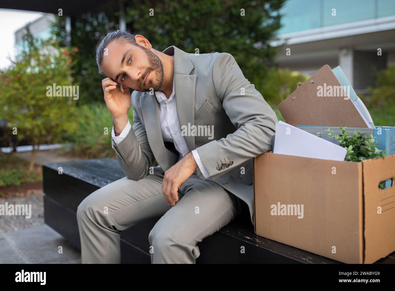 Thoughtful young businessman sitting on bench with a box of personal items Stock Photo