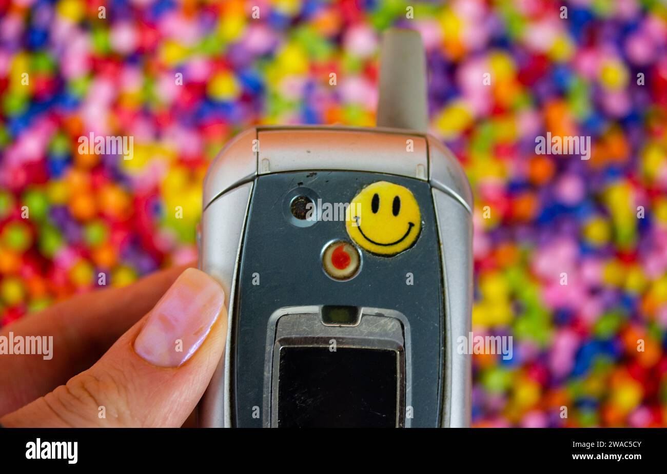 Madrid, Spain. January 2, 2024 Old Motorola phone with smiley face sticker in woman's hand. Nostalgia for '90s, '00s. Hand holding vintage telephone. Stock Photo