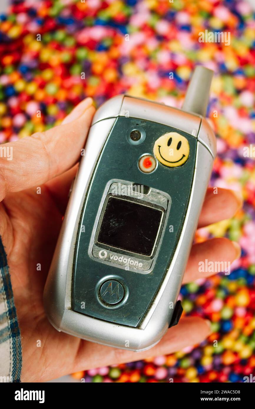 Madrid, Spain. January 2, 2024 Old Motorola phone with smiley face sticker in woman's hand. Nostalgia for '90s, '00s. Hand holding vintage telephone. Stock Photo