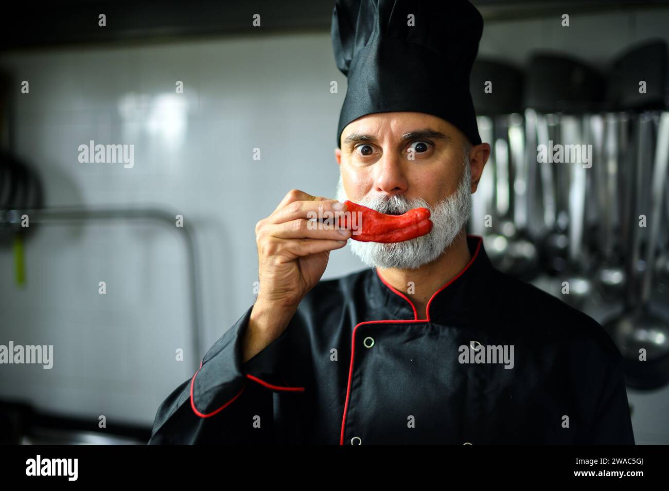 Chef in professional attire humorously poses with a red chili pepper as a mustache Stock Photo