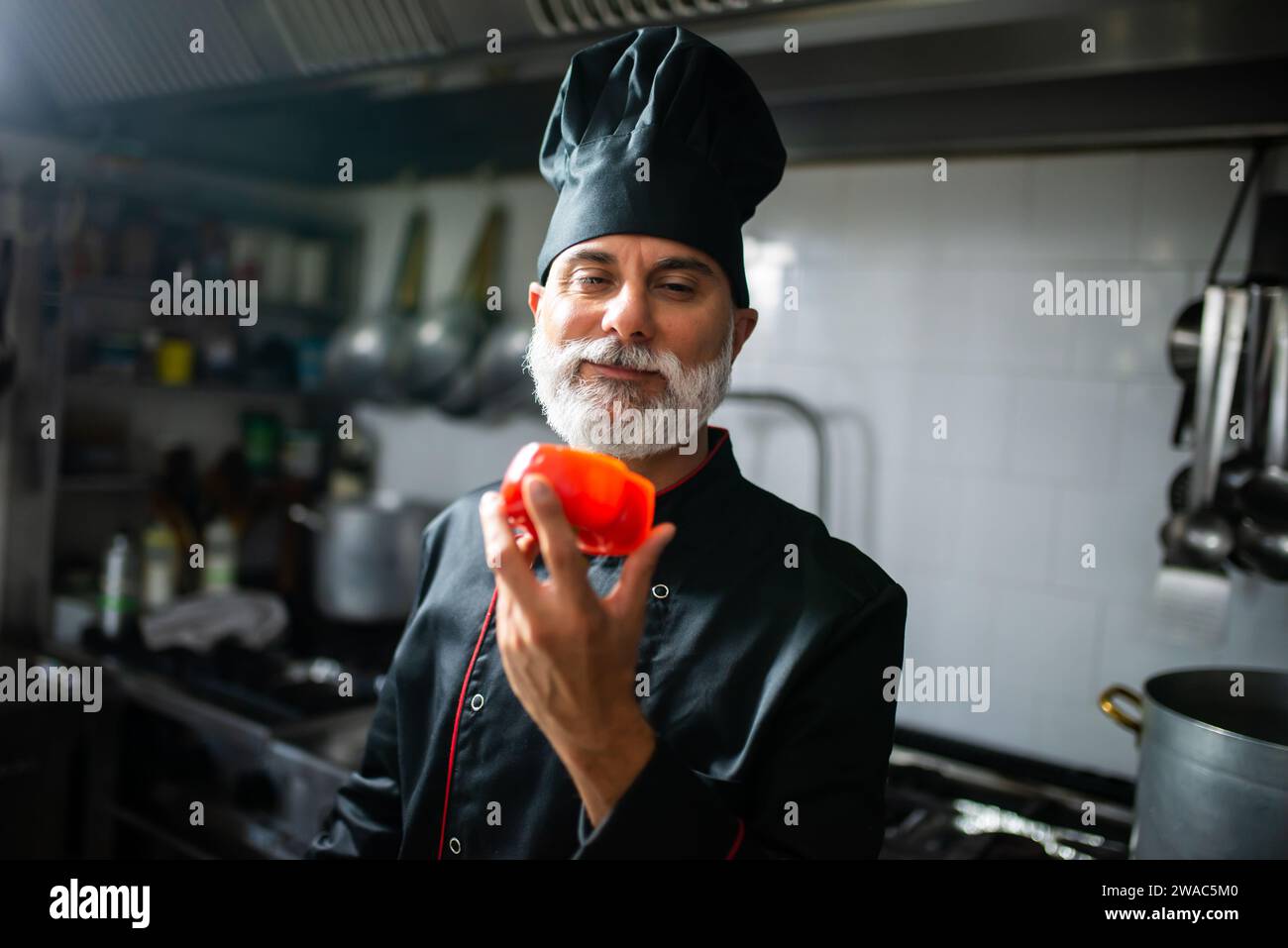 Smiling professional chef in uniform showcasing fresh bell pepper in a commercial kitchen Stock Photo