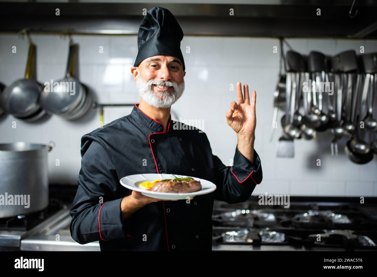 Mature chef holding a meat dish and doing the ok sign Stock Photo