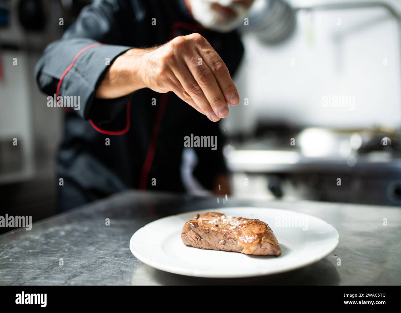 Chef pouring salt on a raw steak to season it Stock Photo