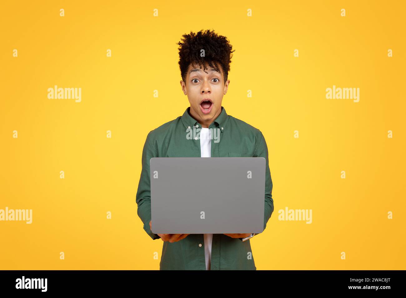 Amazed young black guy using laptop on yellow background Stock Photo
