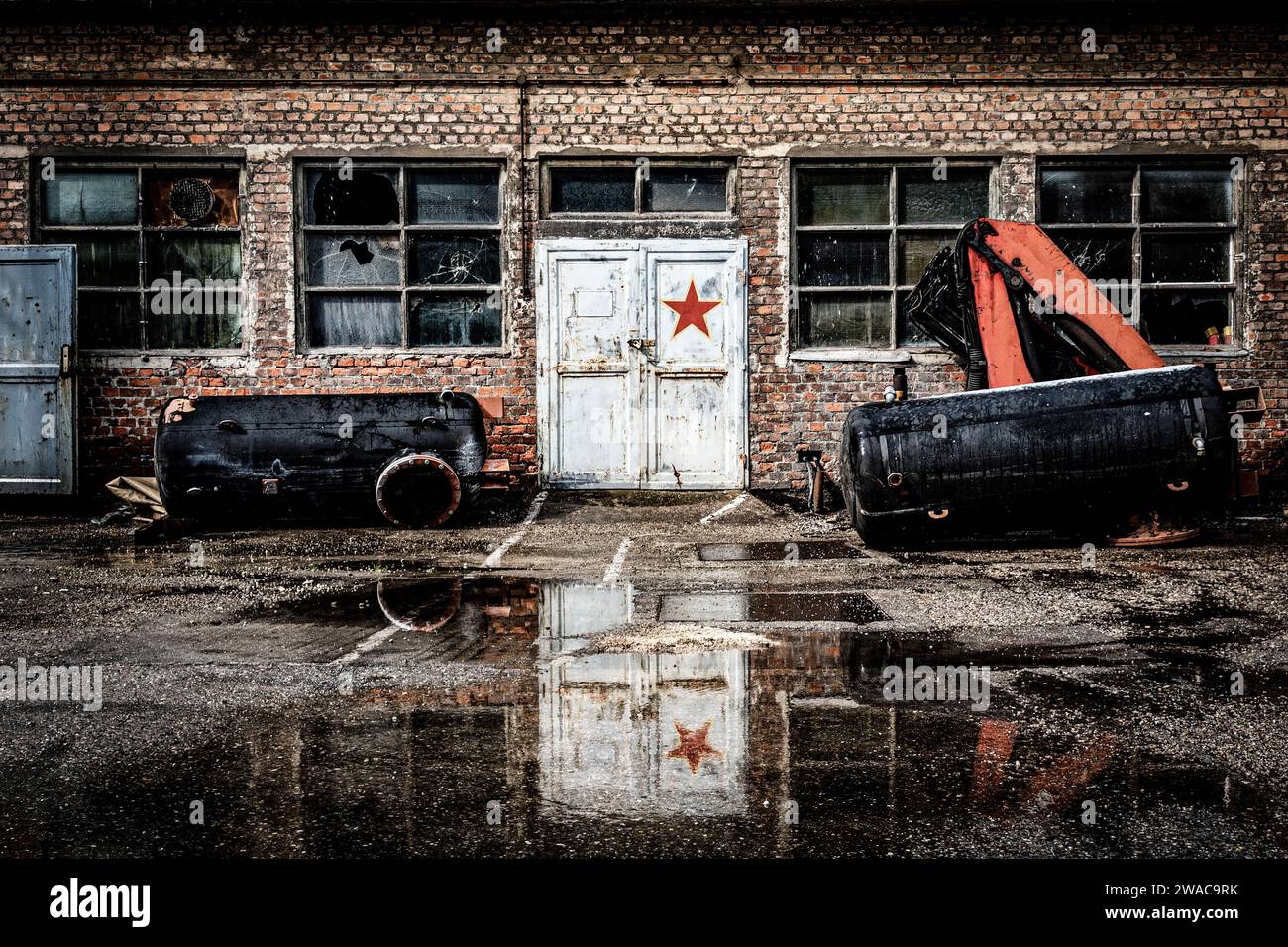 Old dilapidated communist factory with brick walls and broken windows, a door decorated with a red star Stock Photo