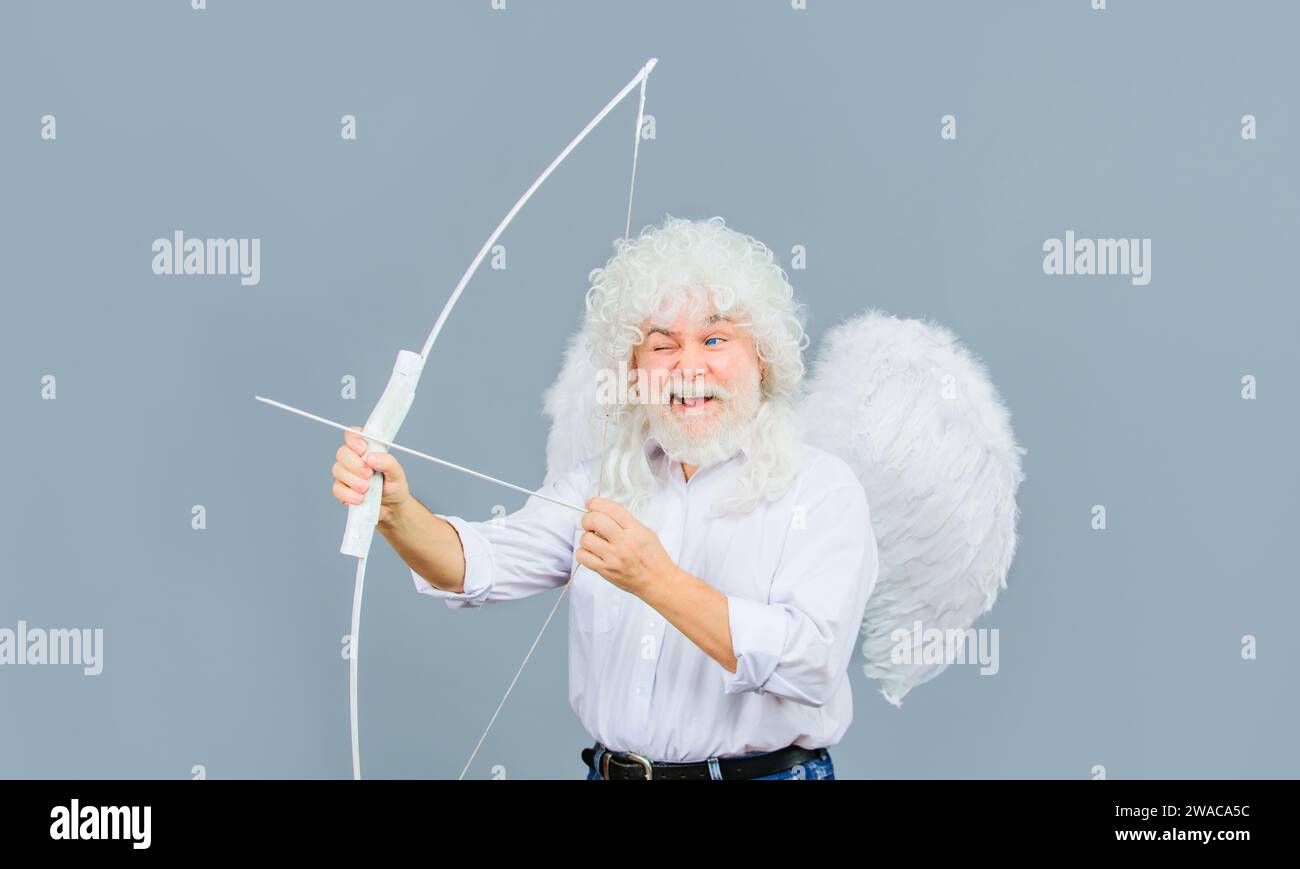 Valentines Day celebration. Happy bearded man in angel wings with bow and arrow. God of love. Valentine cupid in white wig shooting with bow. Arrow of Stock Photo