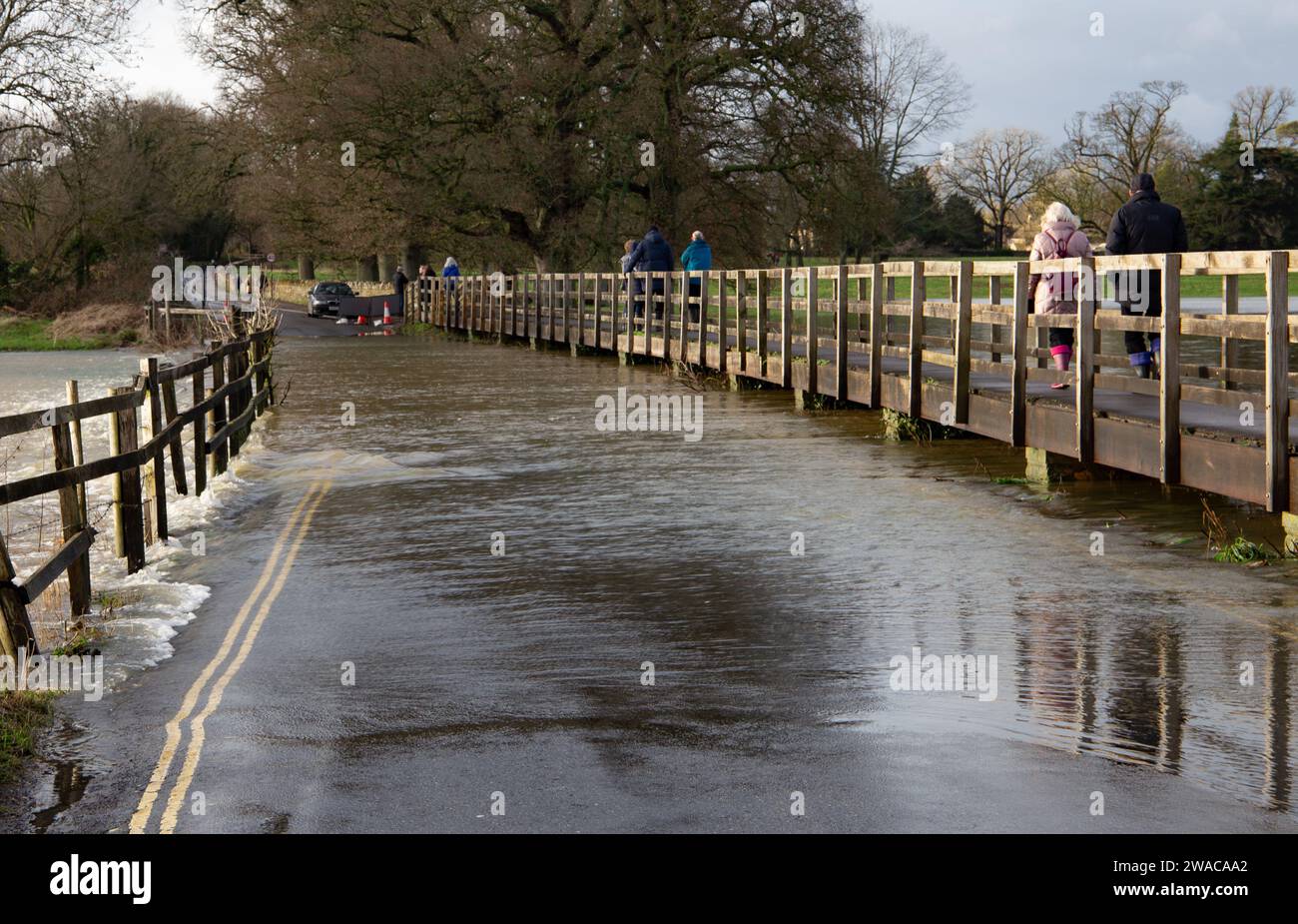 People walking on a raised walkway above the road water flowing underneath after the River Avon burst its banks and flooded road at Lacock Wiltshire Stock Photo