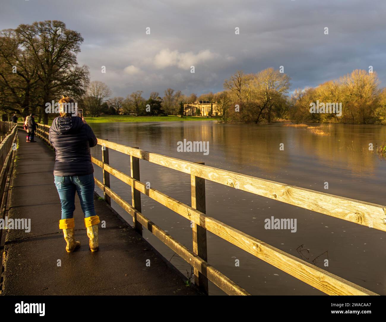 Flooded river Avon at Lacock Wiltshire after storm Henk with the abbey in the background. People walking on the raised path above the flood taking pic Stock Photo