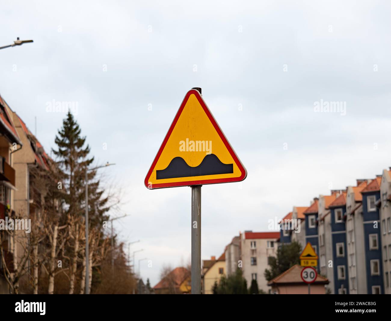 Bumpy road sign in Poland. Drive with caution because of a bad street condition and dangerous circumstances for traffic users or speed ramps. Stock Photo
