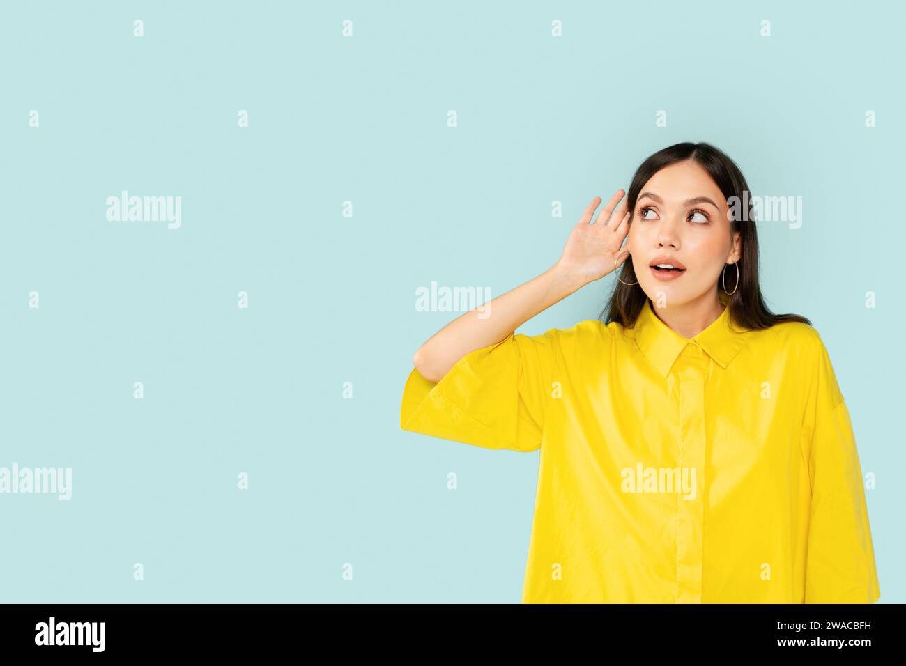 Curious young woman eavesdrop on blue background Stock Photo
