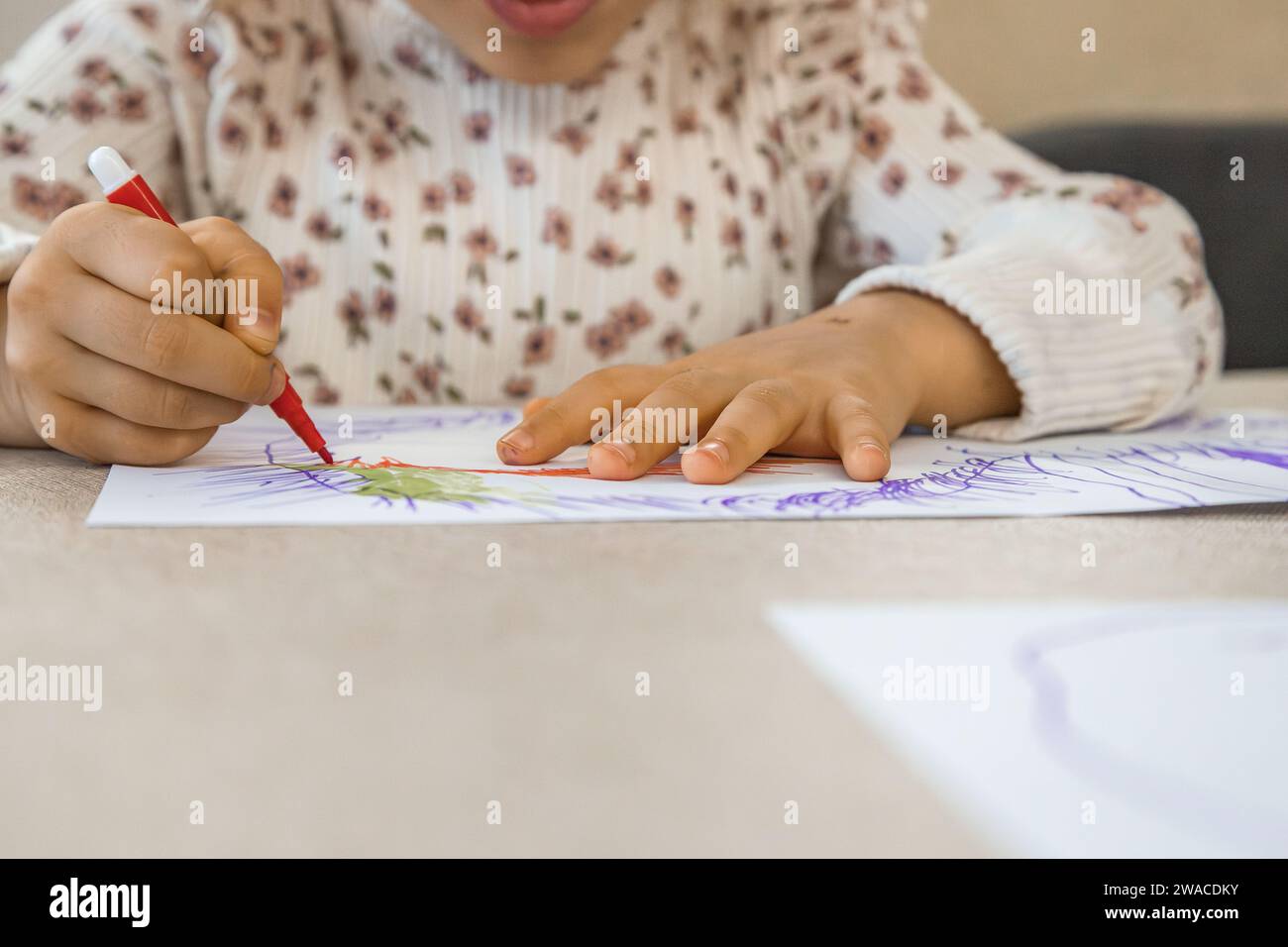 Little caucasian girl painting and drawing on a white sheet with markers, exploring imagination, concentration and agility with her hands. Close up Stock Photo