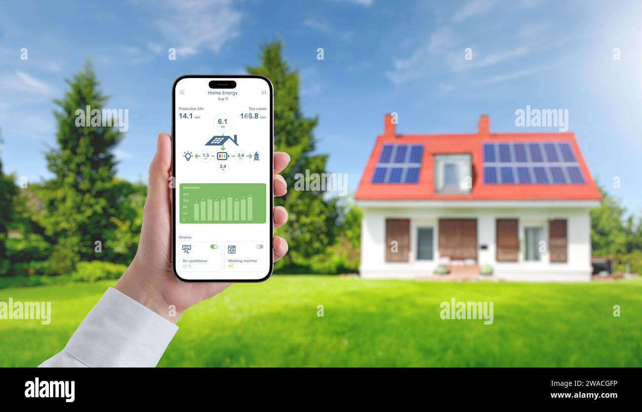 App on a mobile phone monitors the collection and consumption of electricity by solar panels. In the background is a house with solar panels on the ro Stock Photo