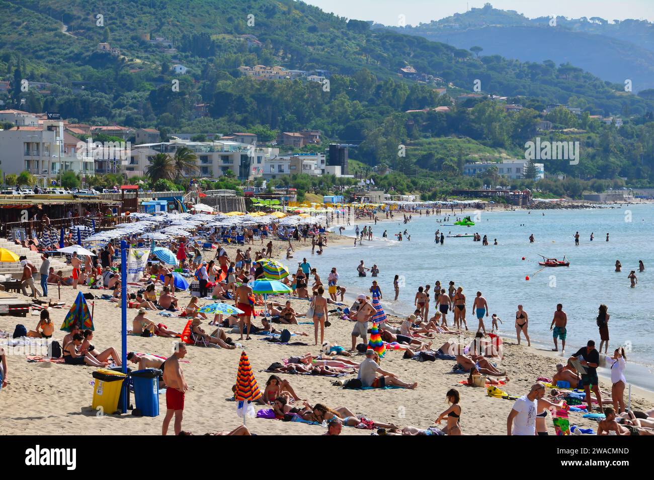 Summer day on a crowded beach in Cefalu with crystal blue water and green hills in the background. Stock Photo