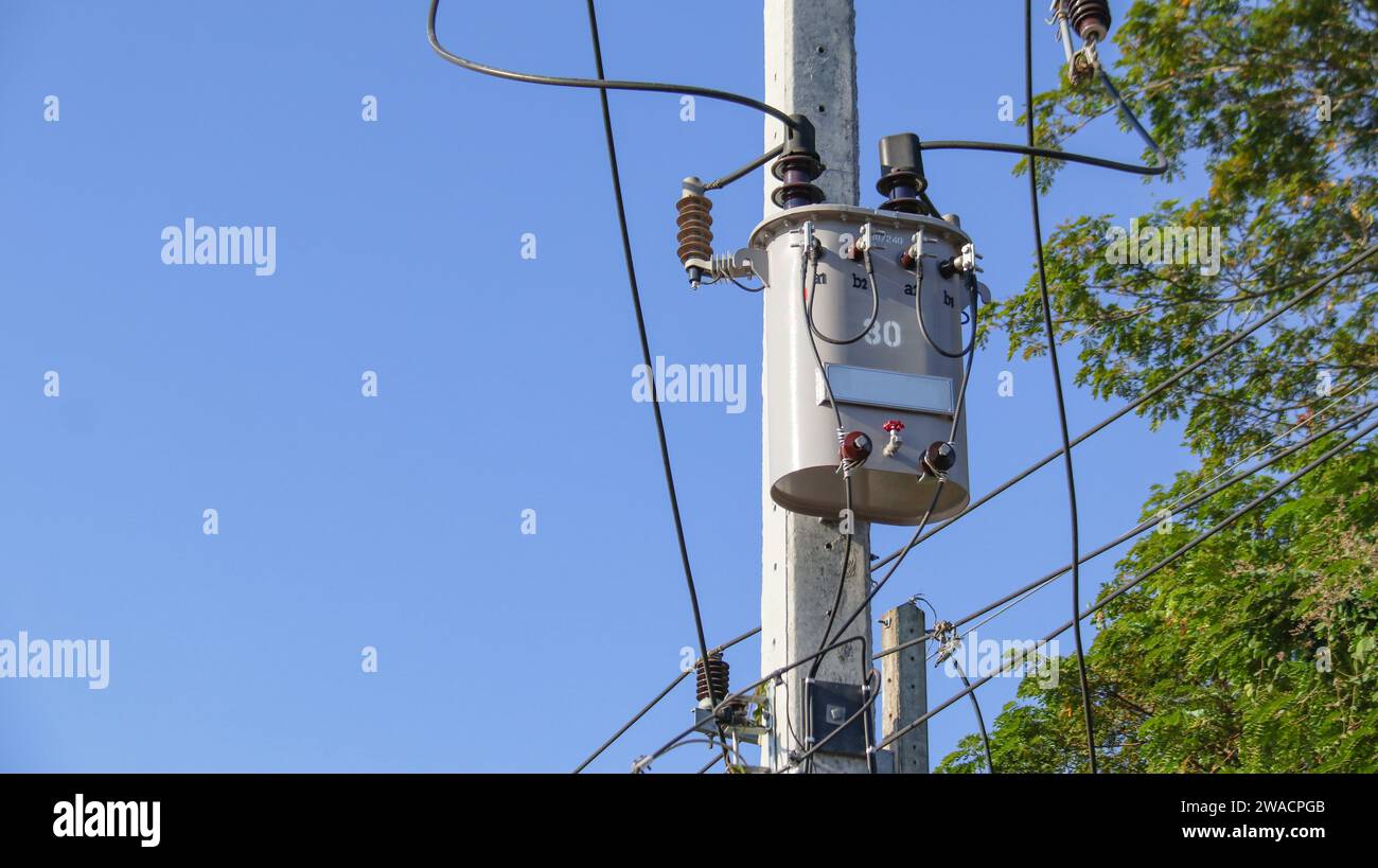 Gray power transformer installed on concrete pole blurred tree and blue ...