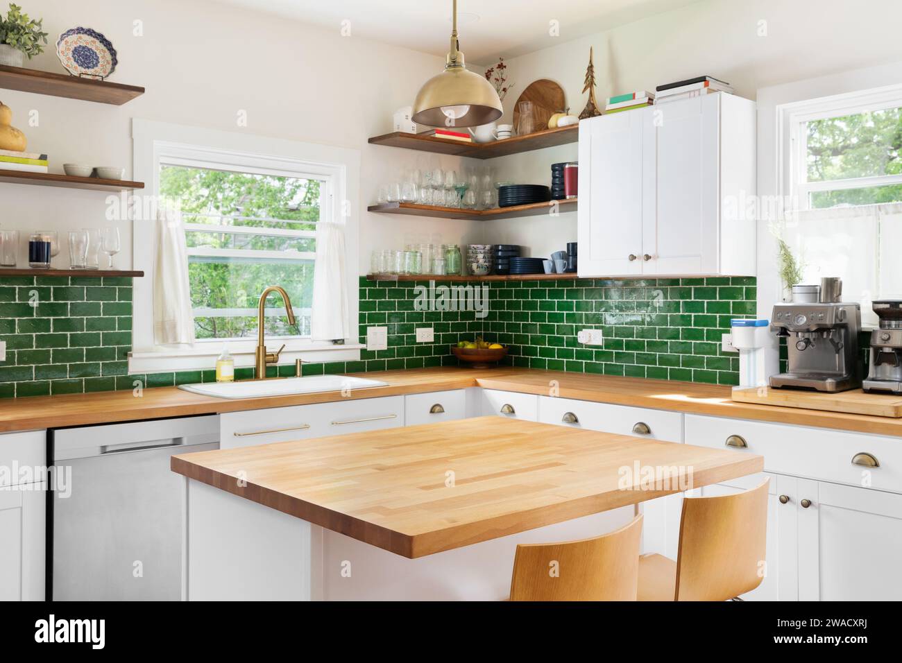 A kitchen detail with butcher block wood countertops, white cabinets, a gold fixture hanging over the island, and green subway tile backsplash. Stock Photo