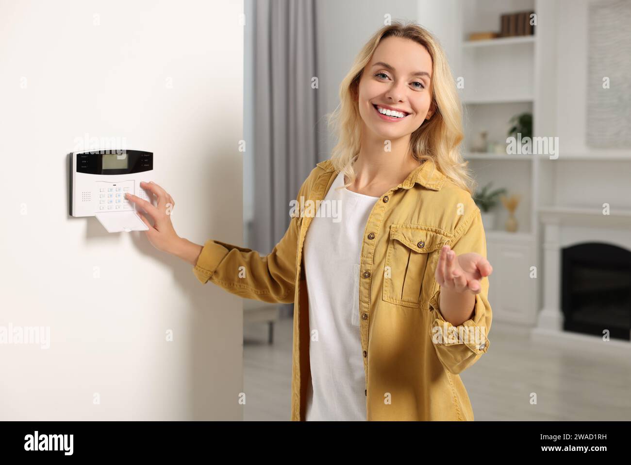 Smiling woman entering code on home security system in room Stock Photo