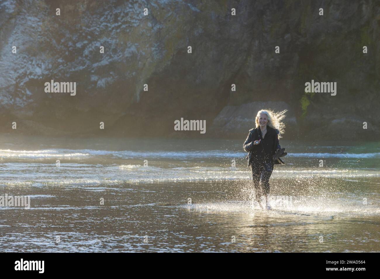 USA, Oregon, Newport, Woman running on sandy beach and splashing water Stock Photo