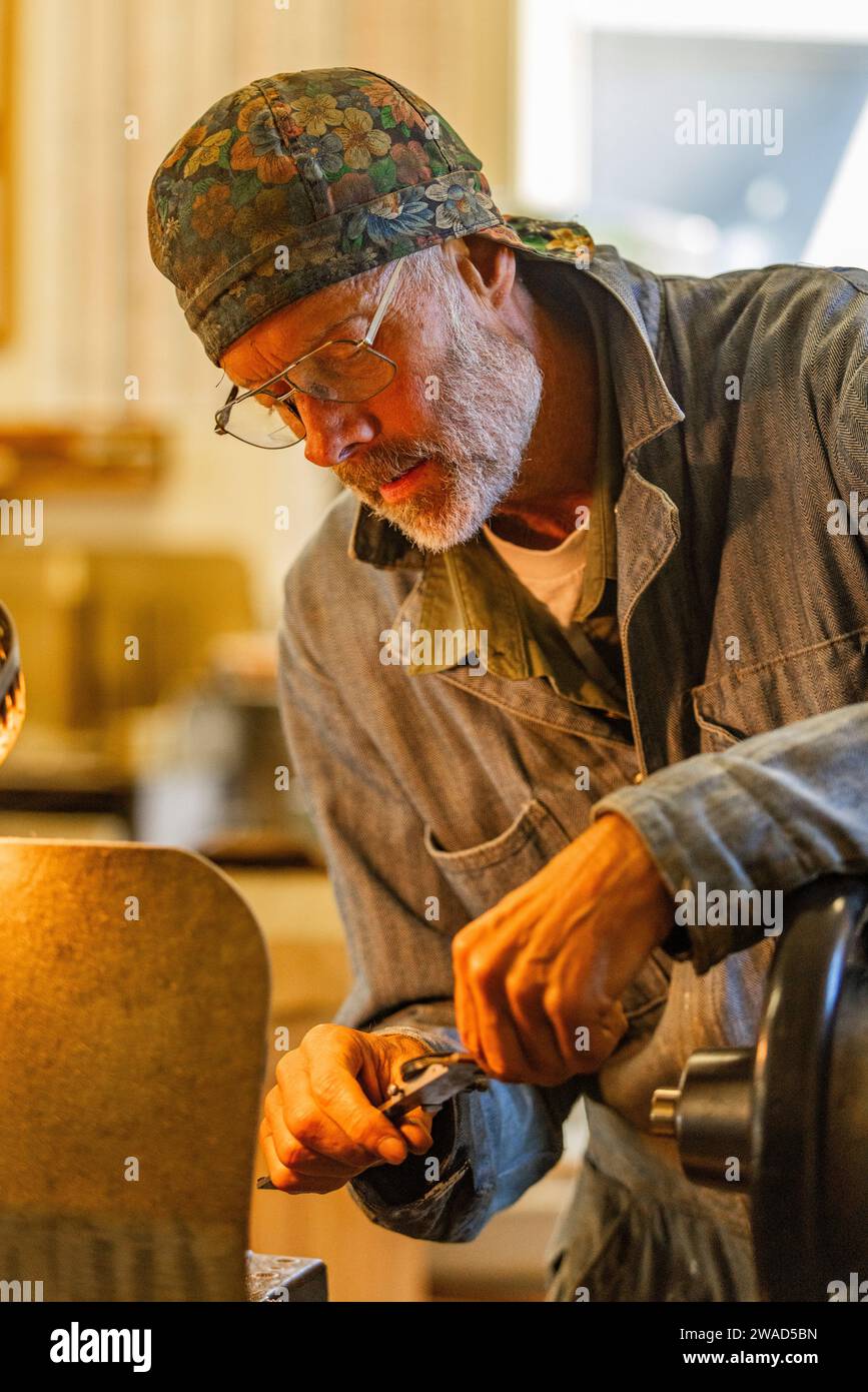 Senior artisan wood and metal craftsman works with tools in workshop Stock Photo