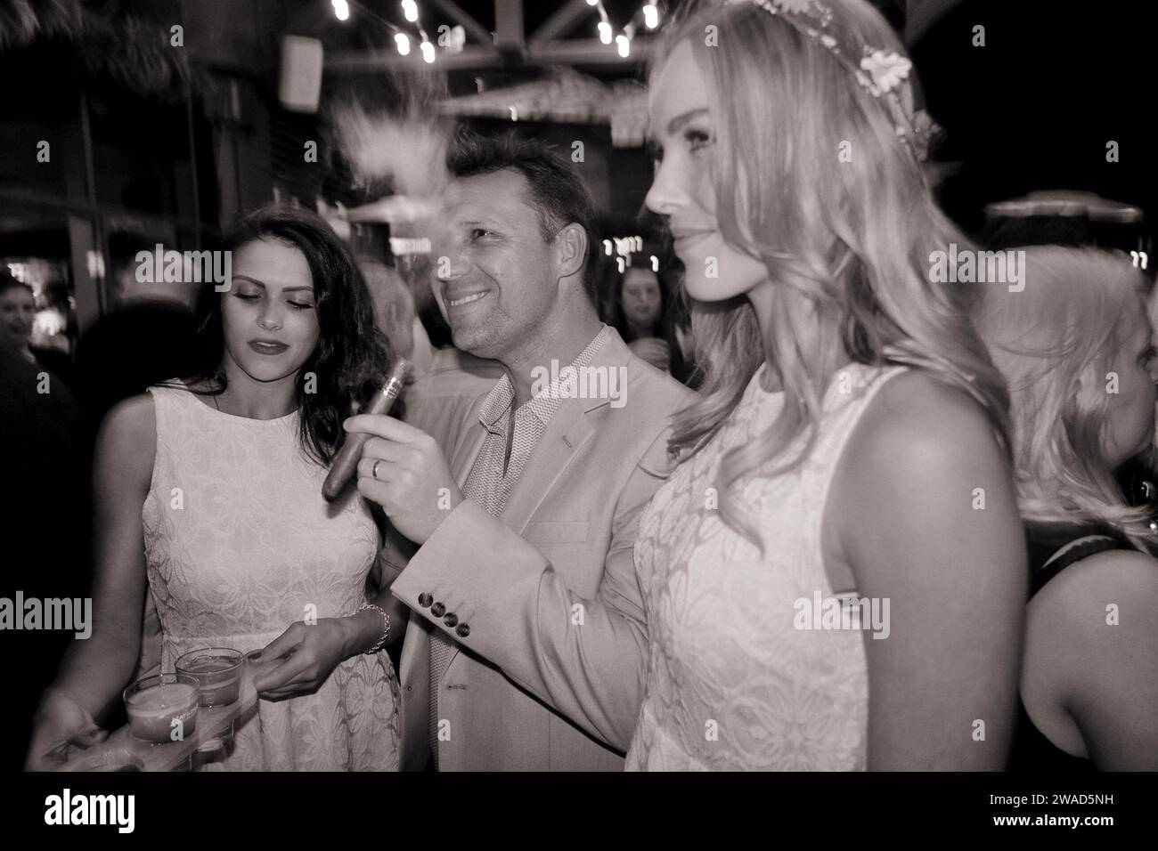 A man smokes a Romeo y Julieta cigar with two beautiful female models by his side at a Havana Cigars event at a Sydney nightclub Stock Photo