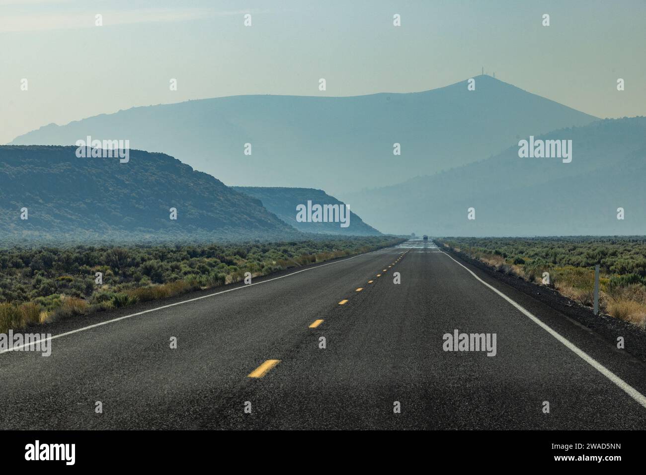 Empty highway leading through desert with mountains in background Stock Photo