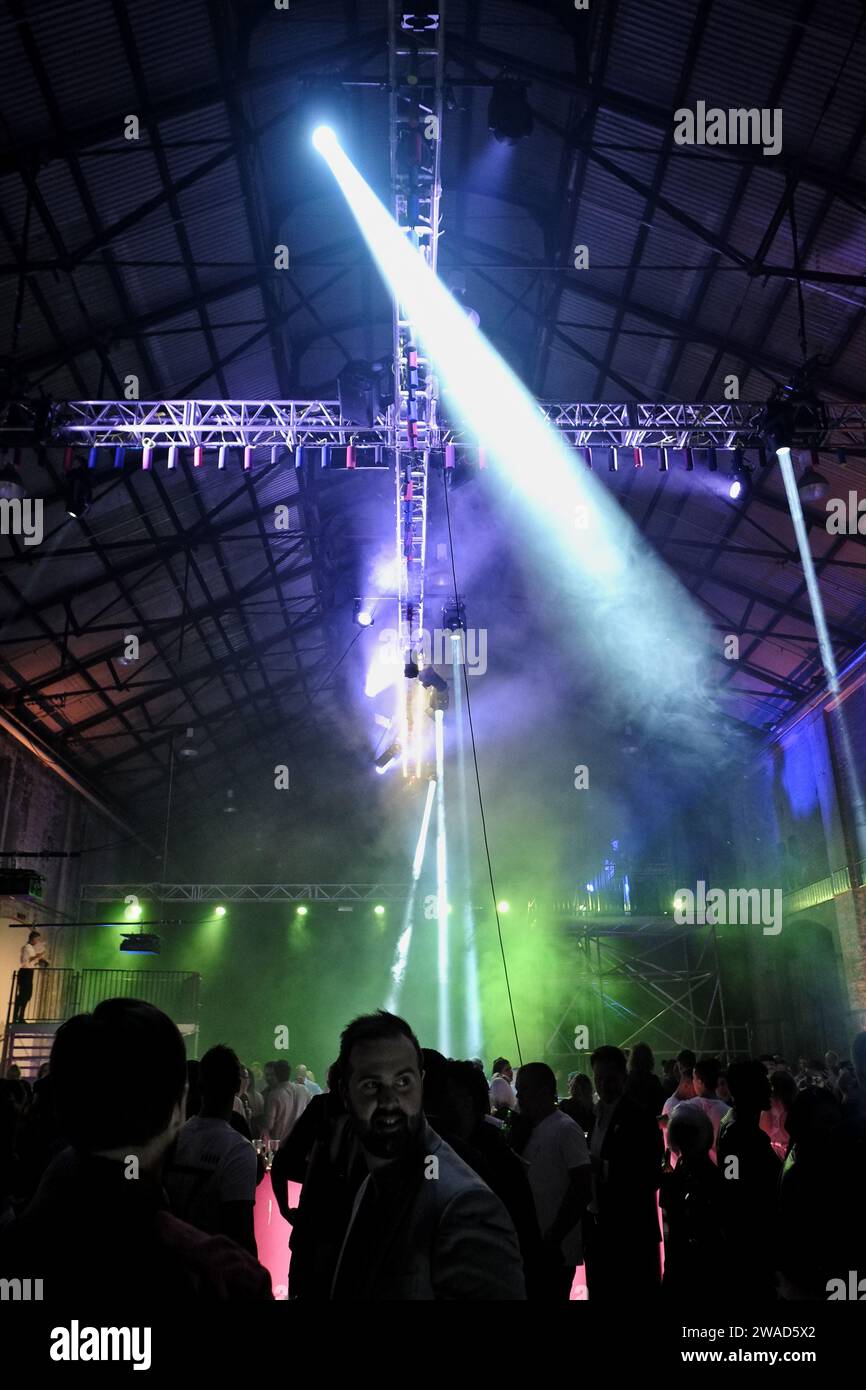 Music party in a large industrial warehouse, small speakers on cross boom rigging overhead, spotlights, green, blue, a crowd of people in silhouette, Stock Photo