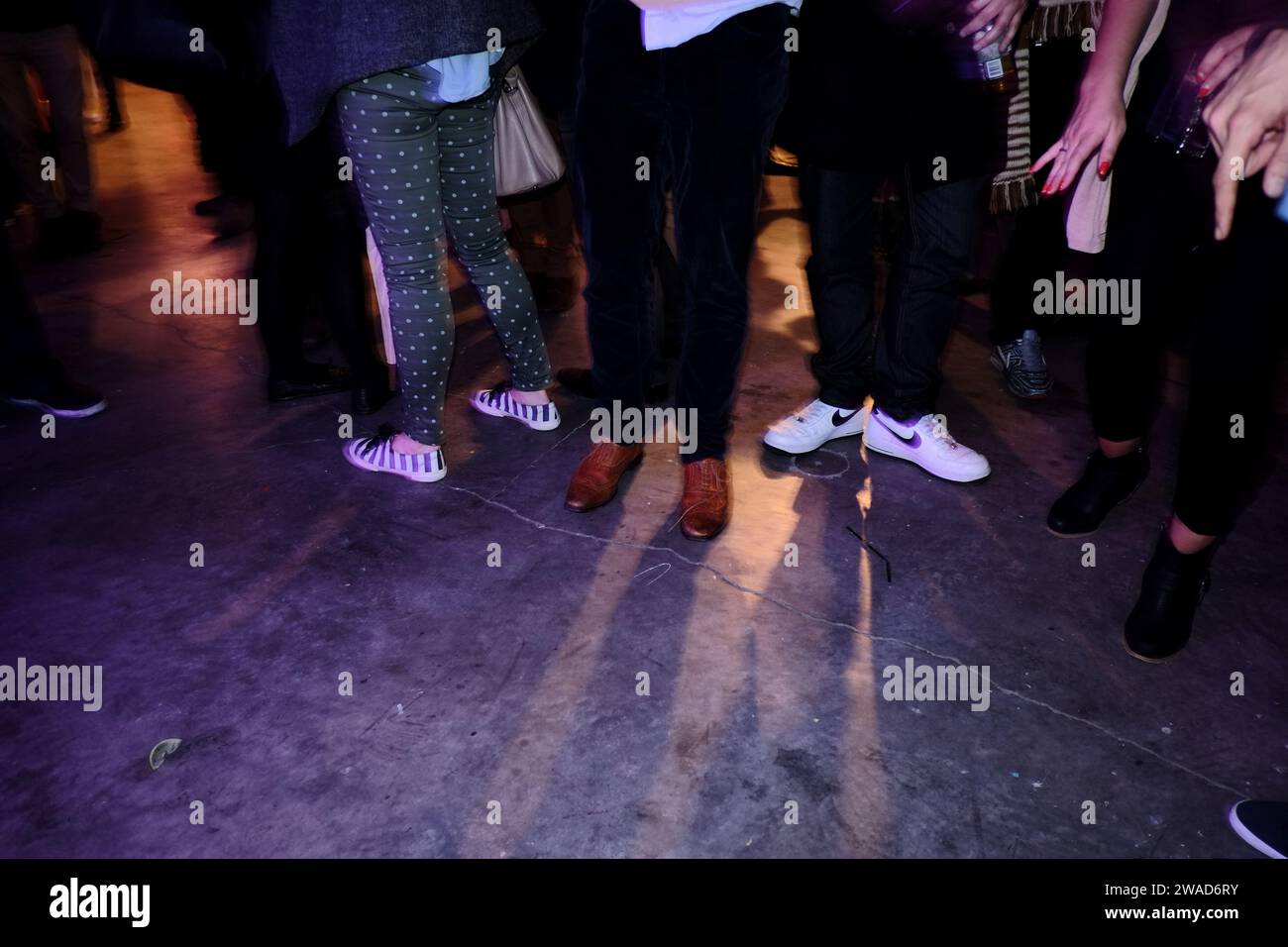 Legs, shoes, runners, sneakers, hands, jeans, pants, coloured light & shadows on a warehouse party dancefloor, nightlife in Sydney Stock Photo