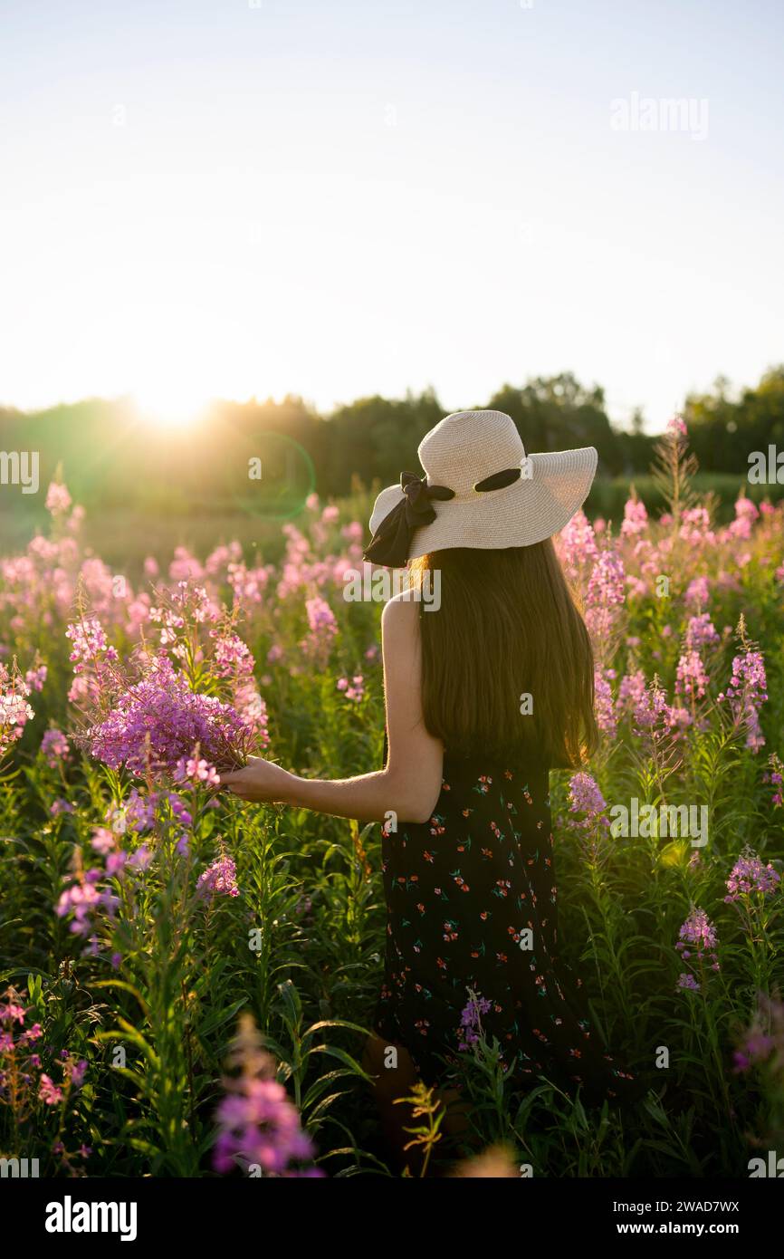 Rear view of woman in straw hat standing in meadow at sunset Stock Photo