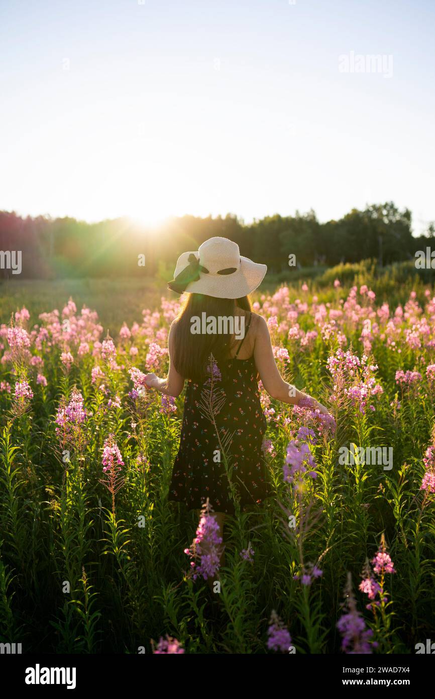 Rear view of woman in straw hat standing in meadow at sunset Stock Photo