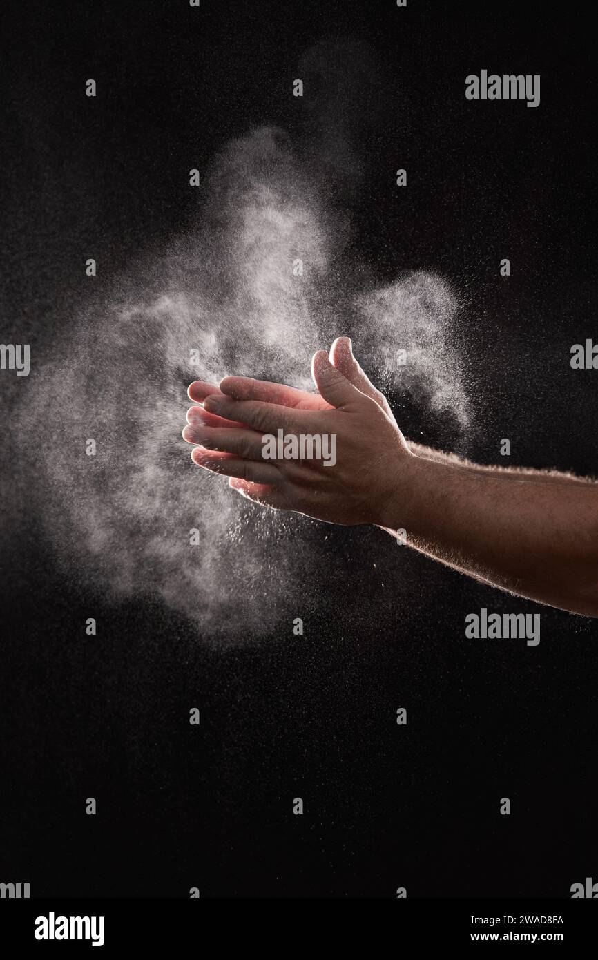 Baker dusting flour off his hands against black background Stock Photo