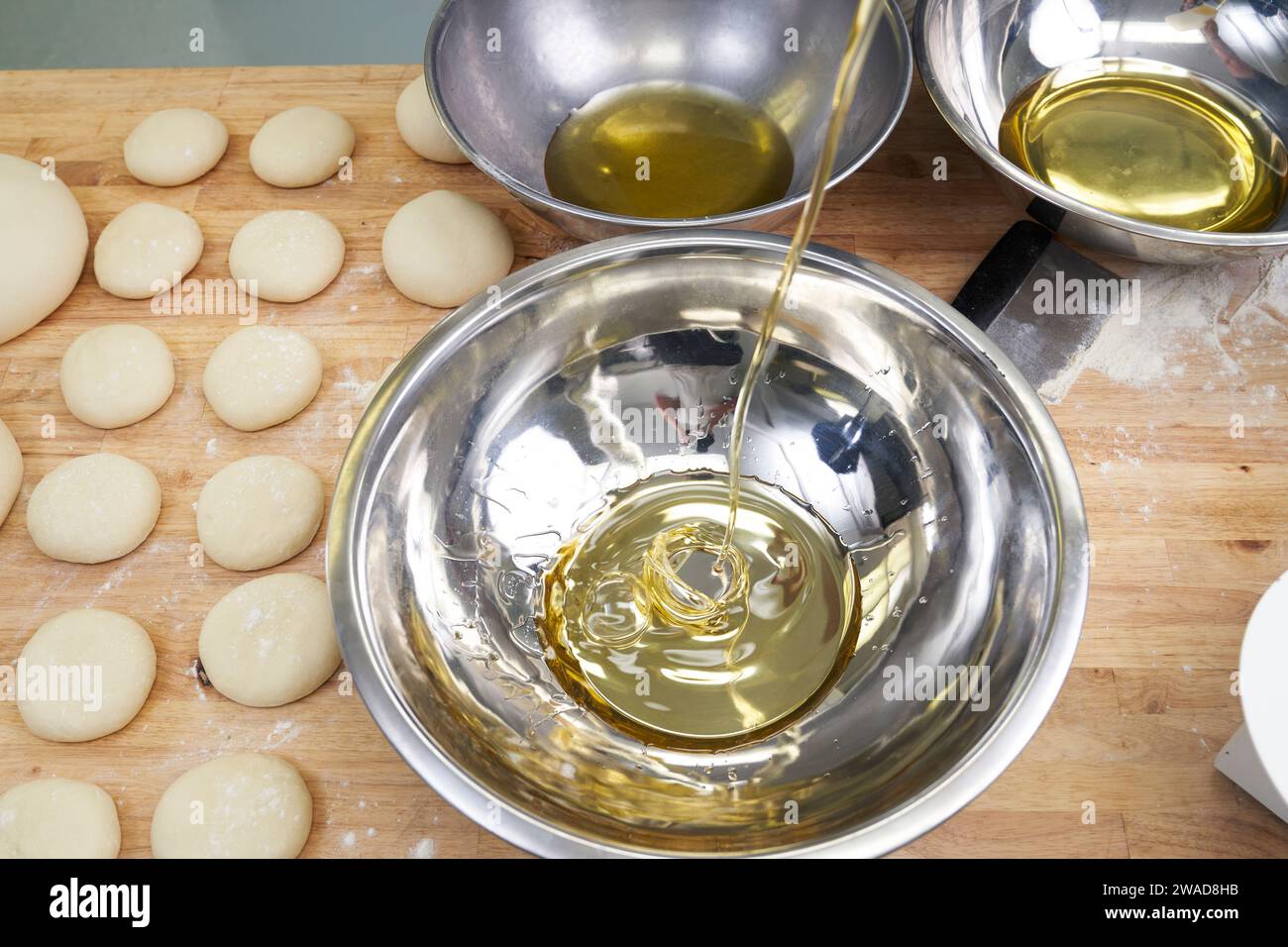 Olive oil pouring into bowl during bread baking Stock Photo