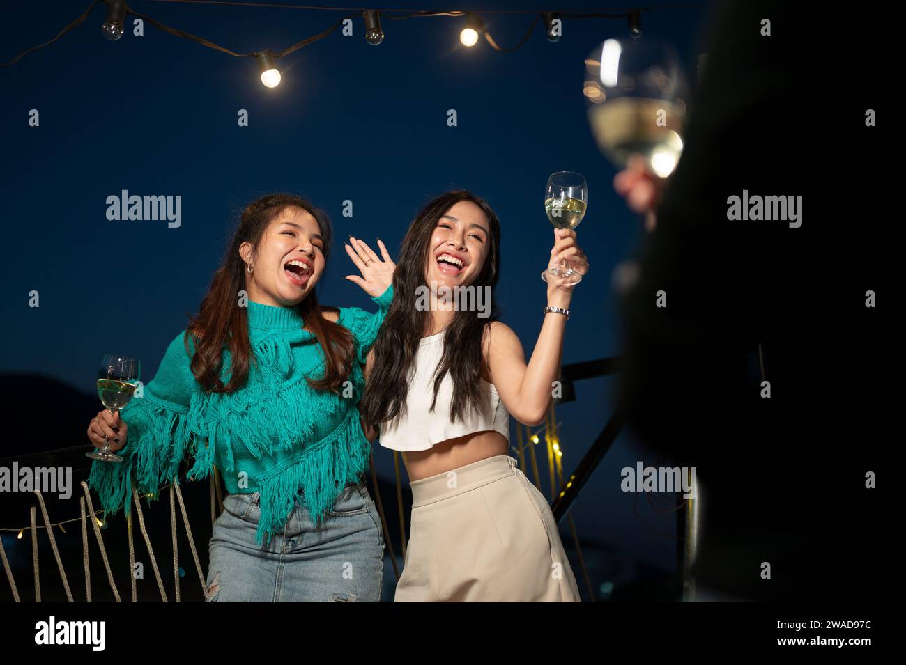 Two attractive, fun Asian female friends are enjoying dancing and drinking champagnes while partying on a rooftop bar together. girls night, city life Stock Photo