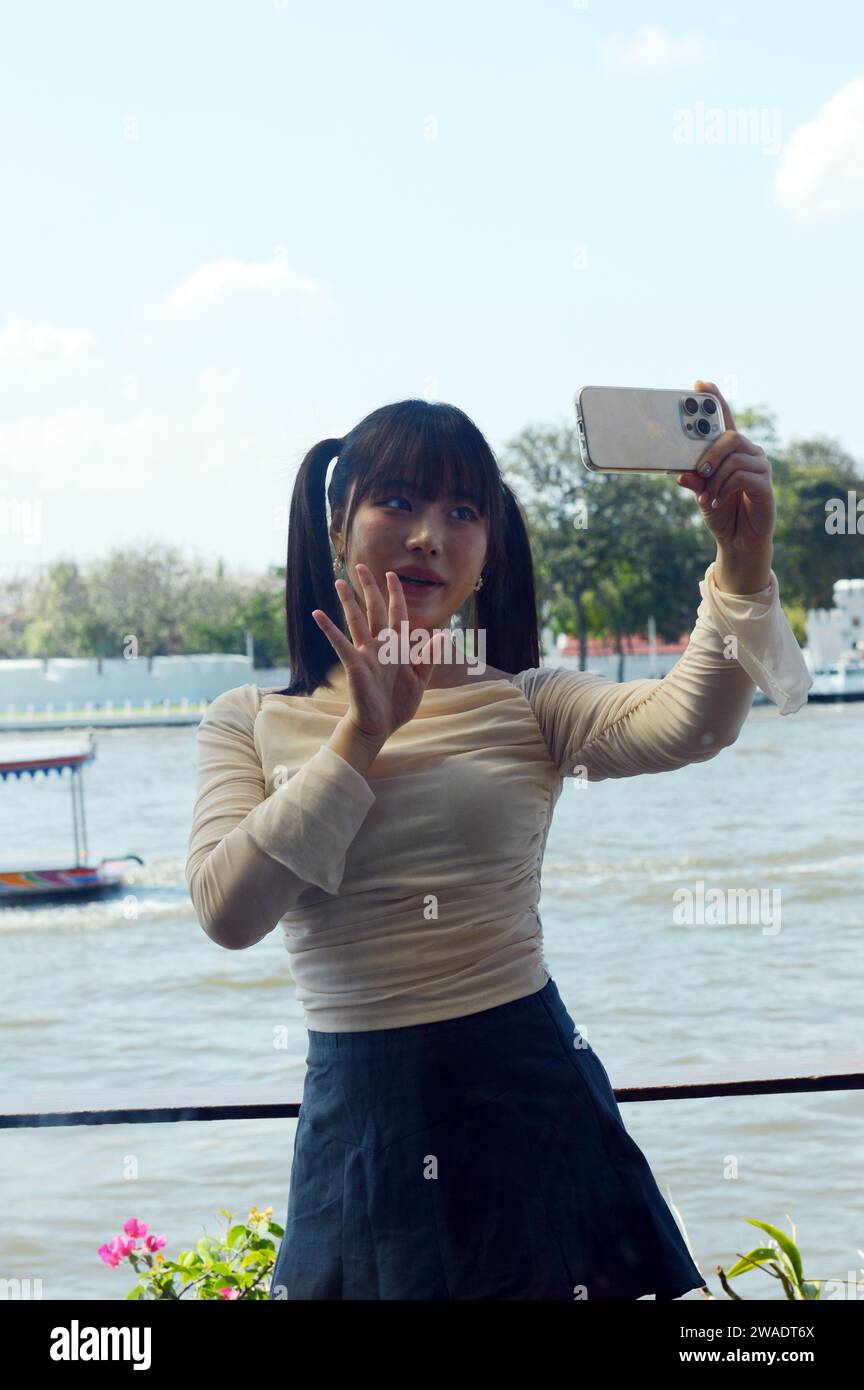 A Gen Z woman posing for selfies and vlogs for her social media by the Chao phraya river in Bangkok, Thailand Stock Photo
