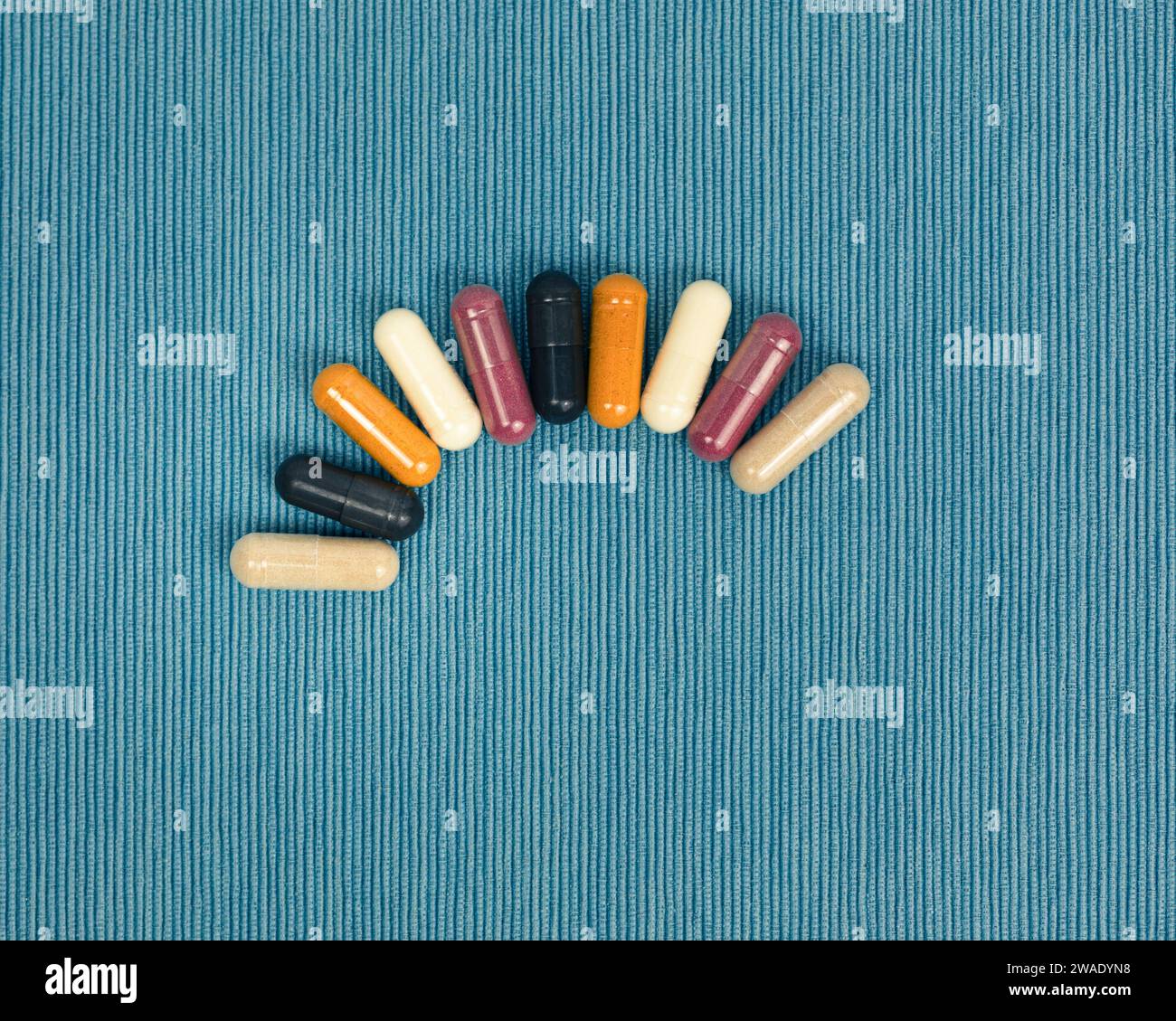 Top view of a variety of vitamin and mineral supplements in capsules. Multicolored pills in orange and red on a blue textured background. Stock Photo