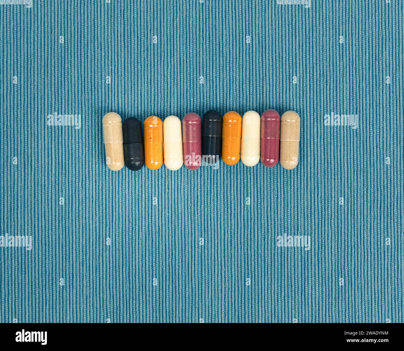 Top view of a variety of vitamin and mineral supplements in capsules. Multicolored pills in orange and red on a blue textured background. Stock Photo